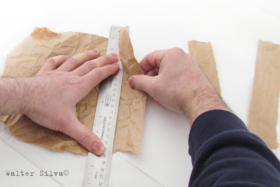 Man's hands ripping a paper bag along a ruler