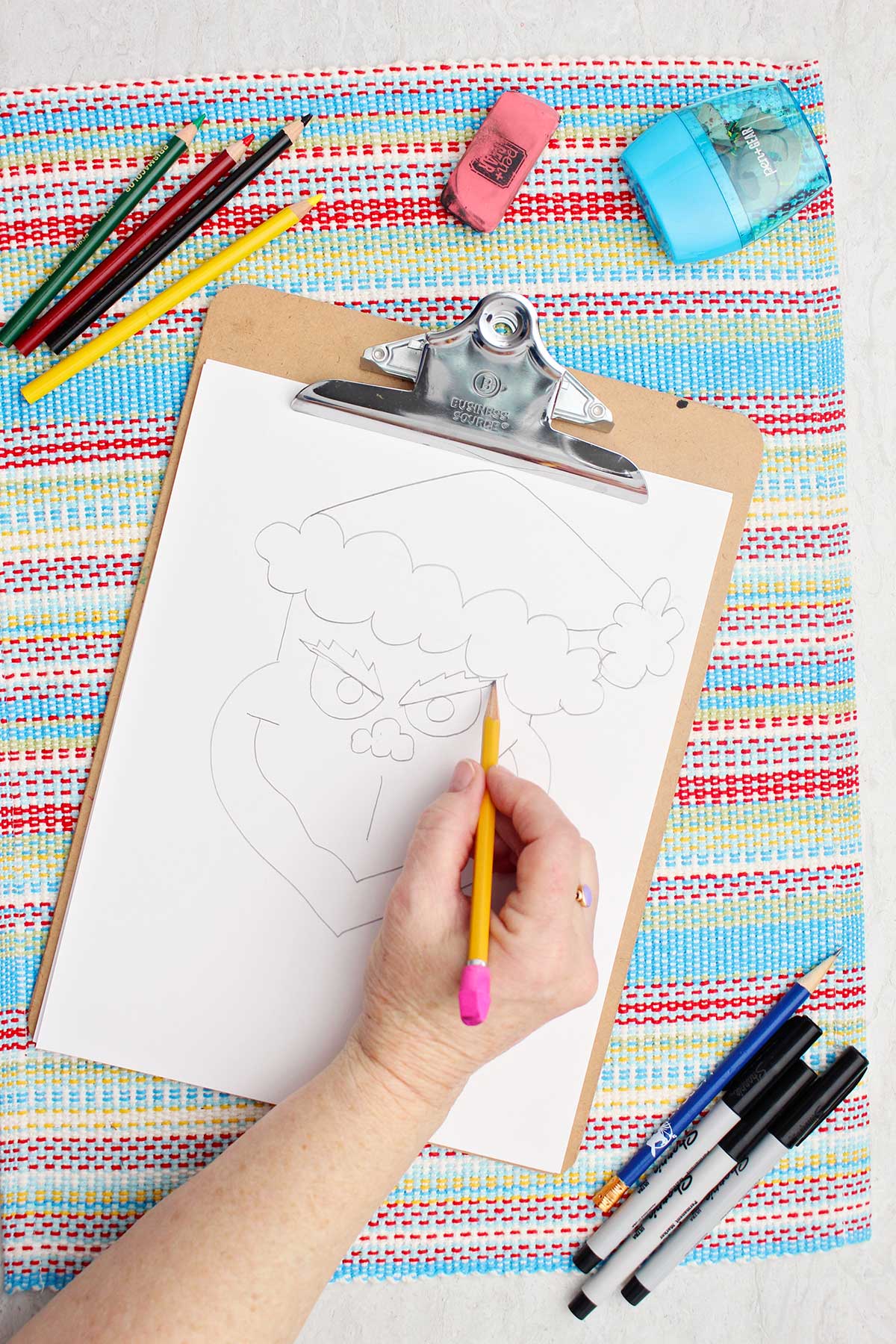 Person illustrating eyebrows on Grinch sketch.