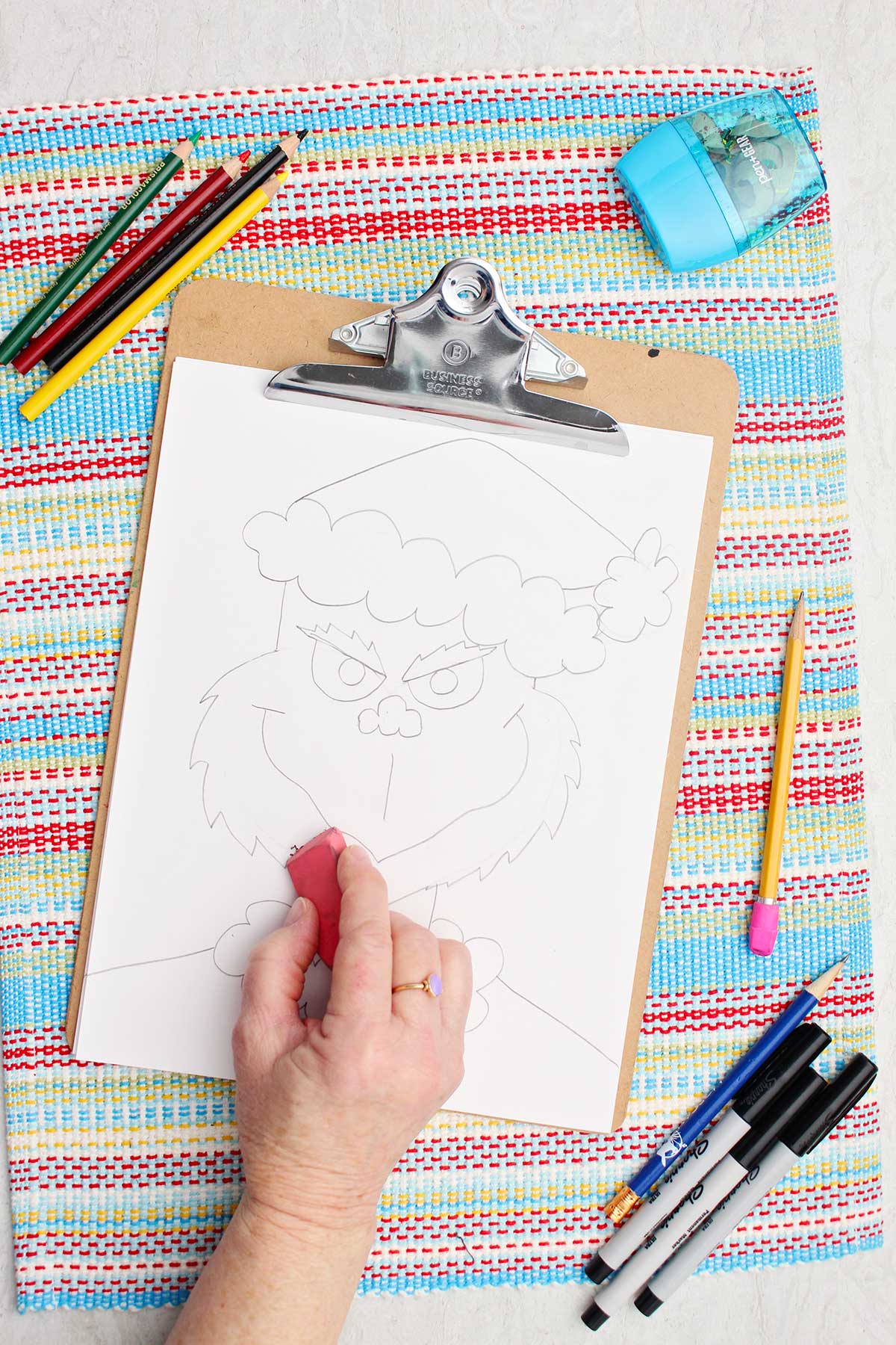 Person tidying up some outlines with a pink eraser on their Grinch sketch.