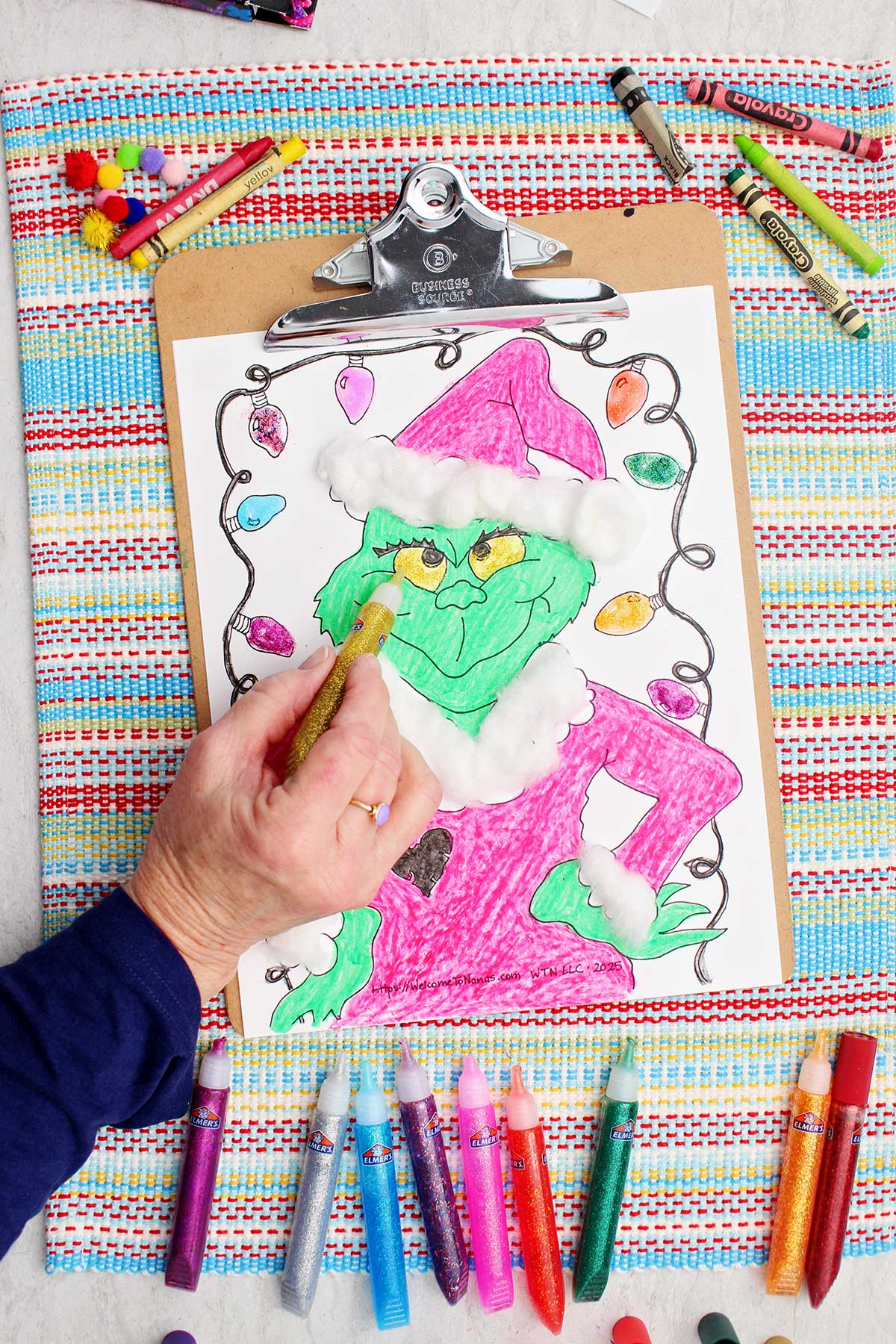 Individual applying gold glitter glue to the Grinch's eyes.