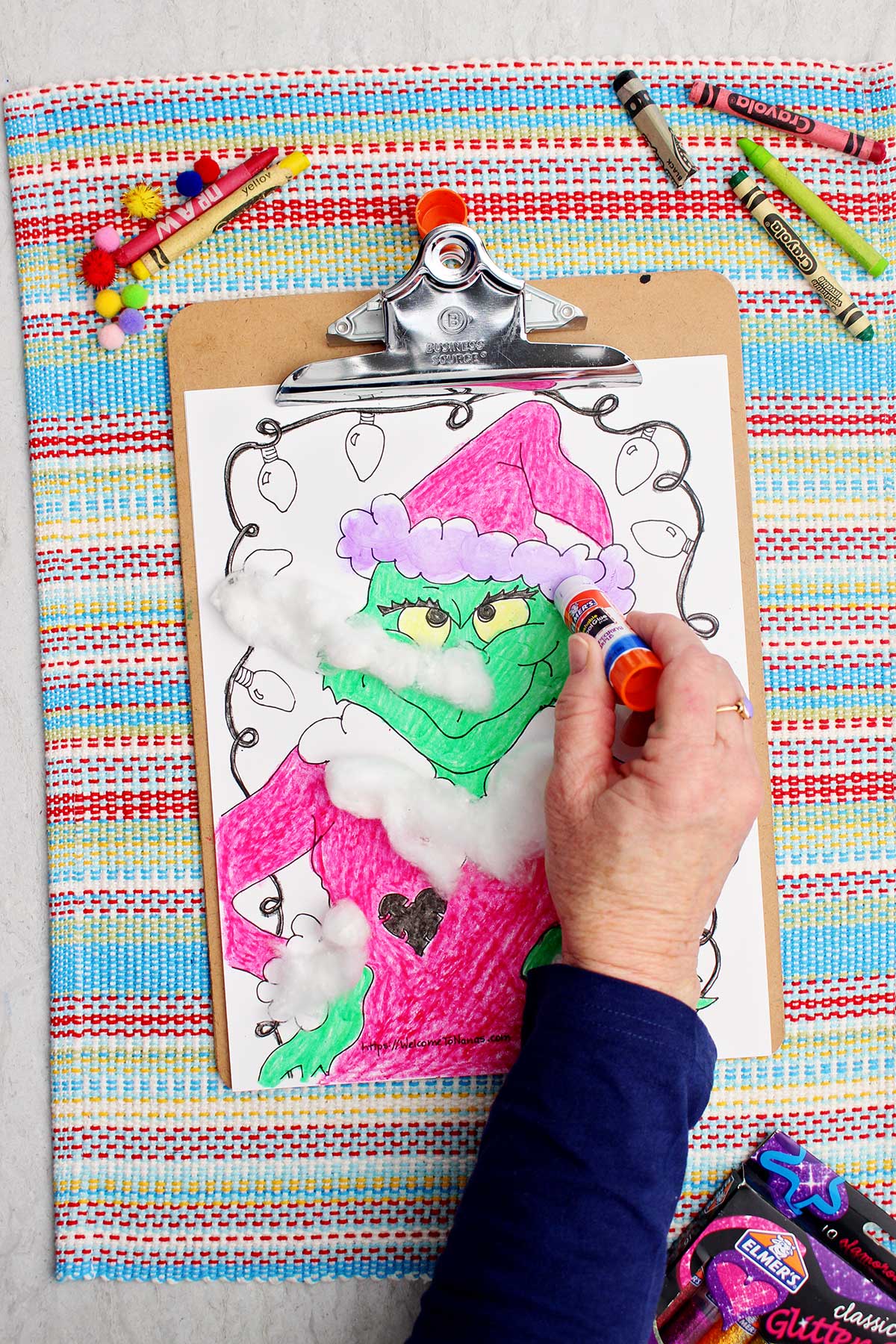 Individual applying purple glue stick on Santa hat accent for affixing cotton balls.