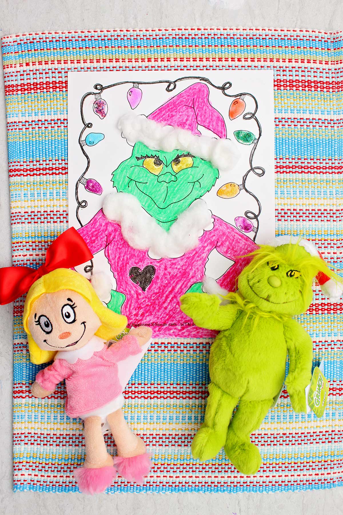 Completed Grinch coloring page with two Grinch stuffed animals nearby.
