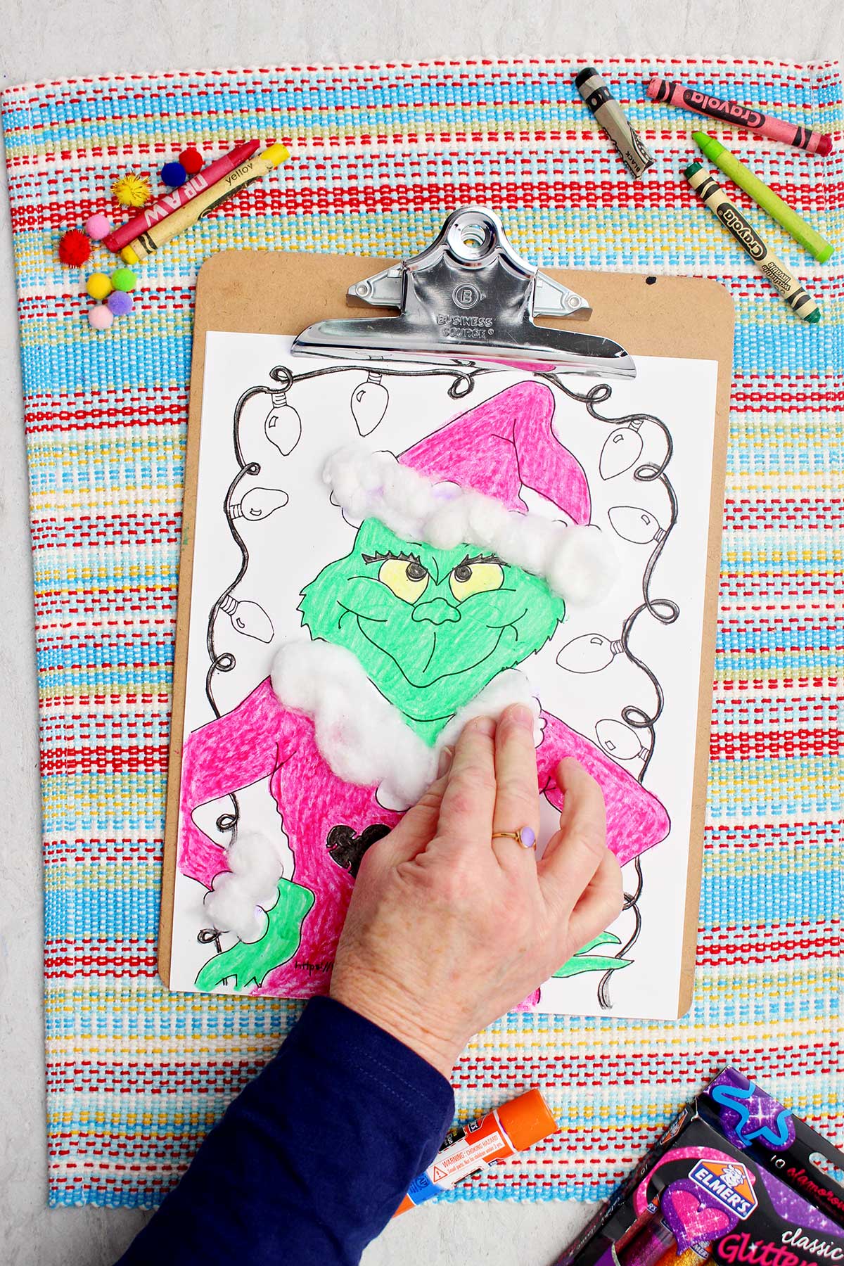 Individual placing cotton balls on accents of Santa coat on Grinch coloring page.