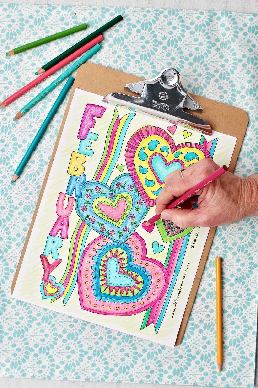 Hand coloring a pink heart on a nearly completed coloring page.
