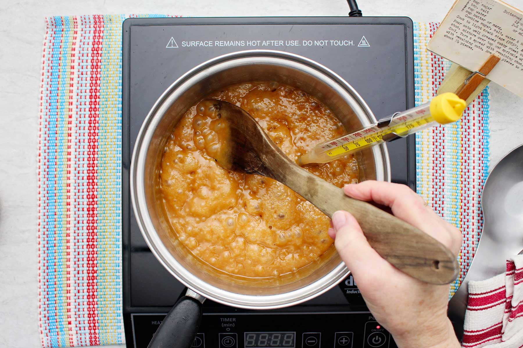 Individual mixing darkening bubbling toffee blend in a saucepan.