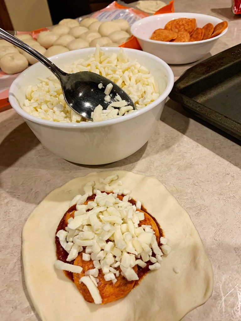 A spoon adding mozzarella into an open pizza pocket.