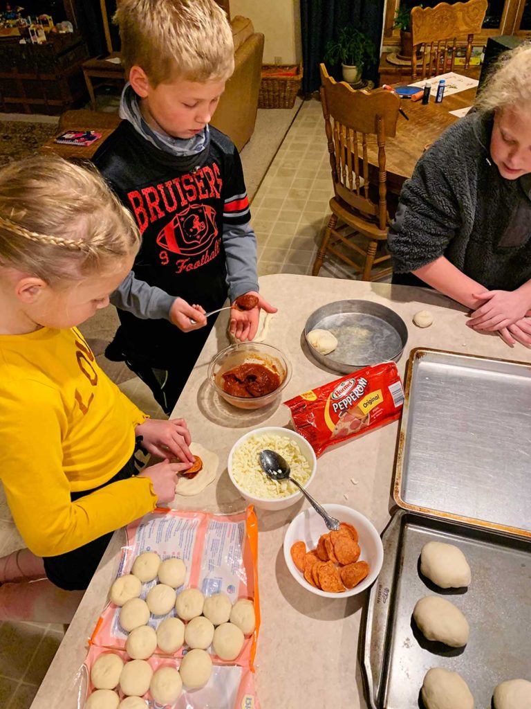 Kids adding marinara, cheese, and pepperoni to spread dough to form pizza pockets.