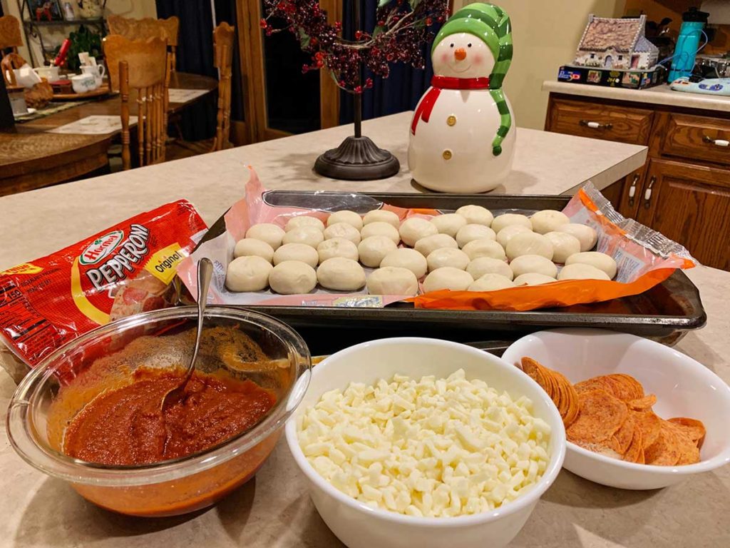 Marinara sauce, mozzarella cheese, pepperoni, and dough balls displayed on a countertop.