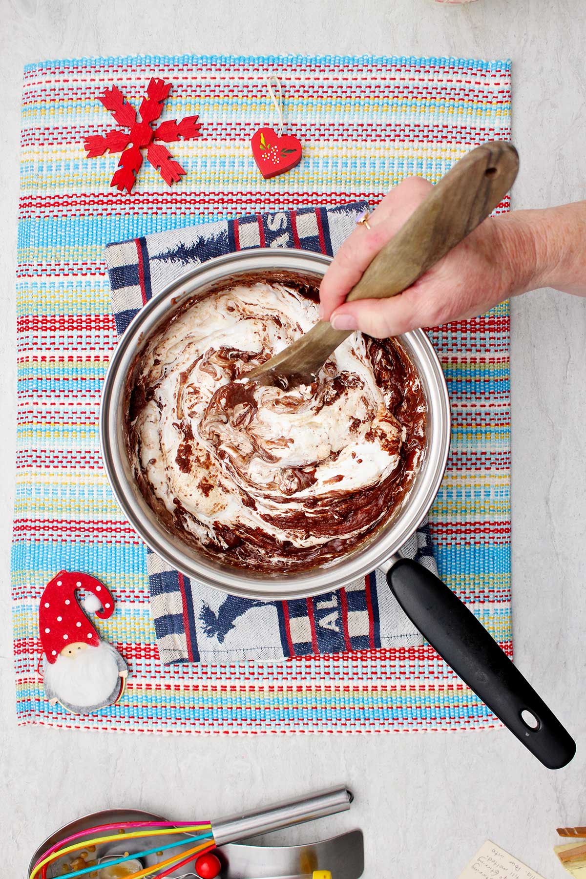 A person stirring the fluff and chocolate fudge mixture off heat on a colorful placemat.