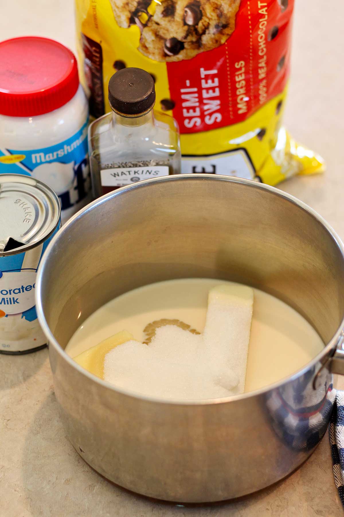 A pot filled with evaporated milk, butter, and sugar with additional ingredients in the background.