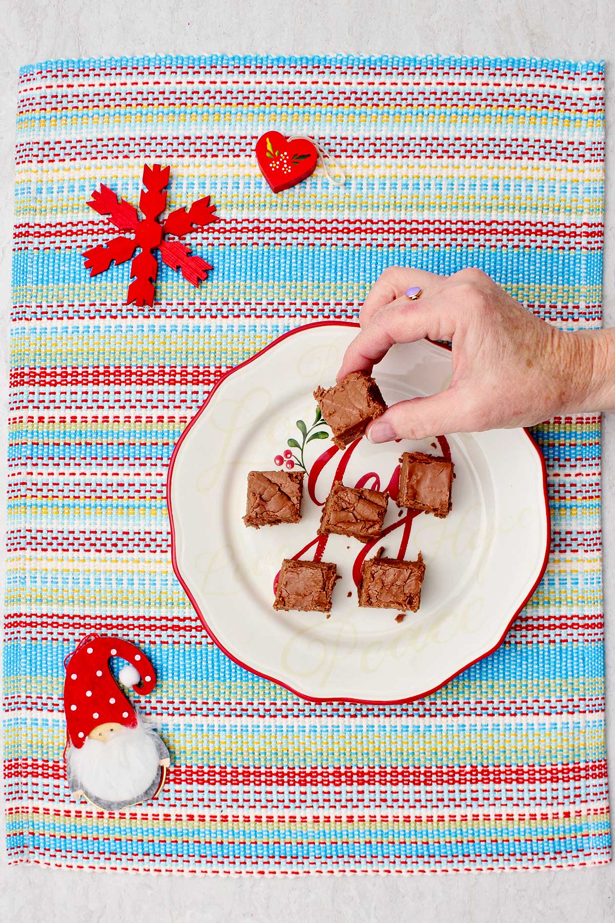 An individual lifting a piece of fudge from a festive plate.