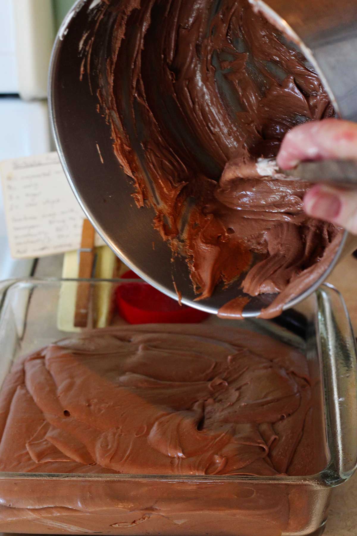 Person scooping fudge mixture from saucepan into glass baking pan.