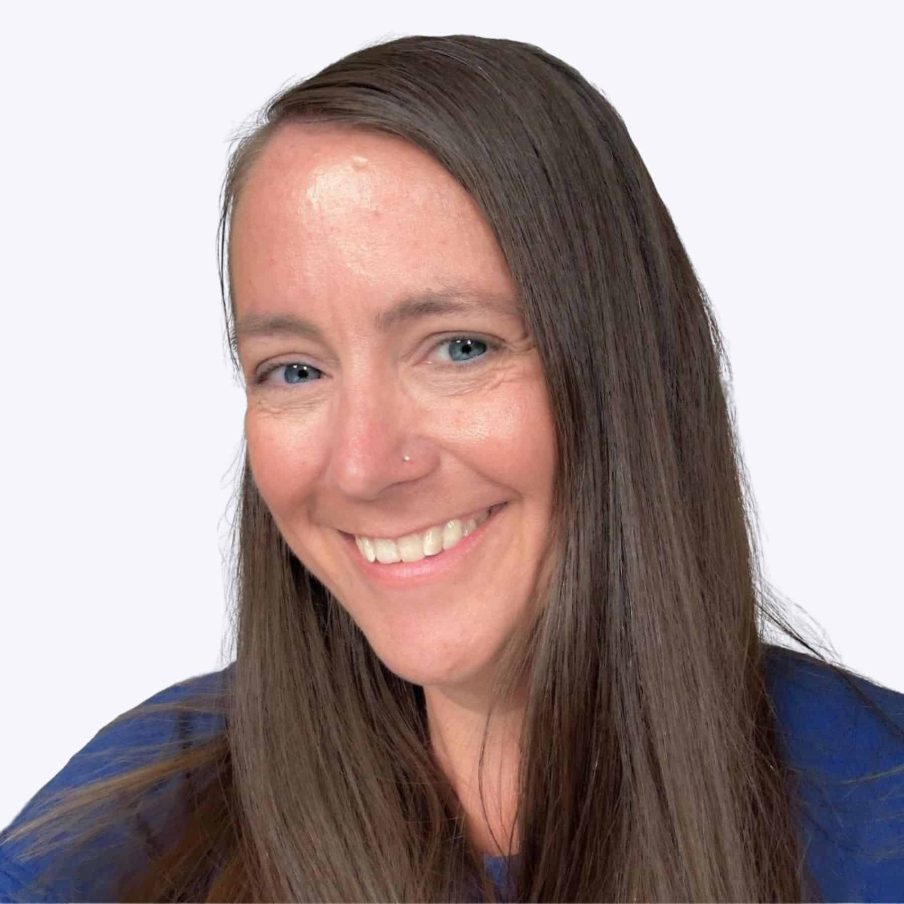 Close-up portrait of a grinning woman with long straight hair and a nose ring, dressed in a dark outfit against a simple backdrop.