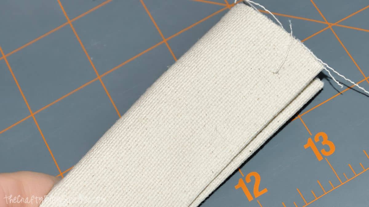 step 9 b Folded canvas strap with stitched edges displayed on a cutting mat during the construction of a handmade tote bag strap.