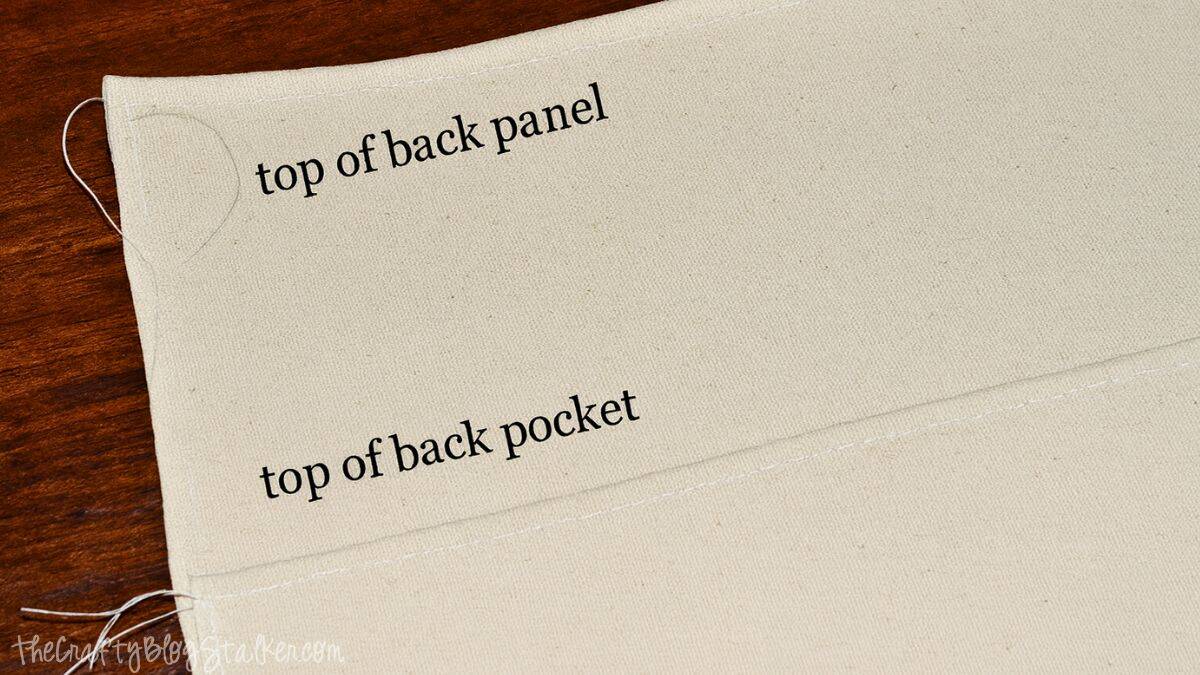 Step 1_edited-1 Canvas fabric segments marked top of back panel and top of back pocket displaying folded hems for sewing a crochet tote bag.