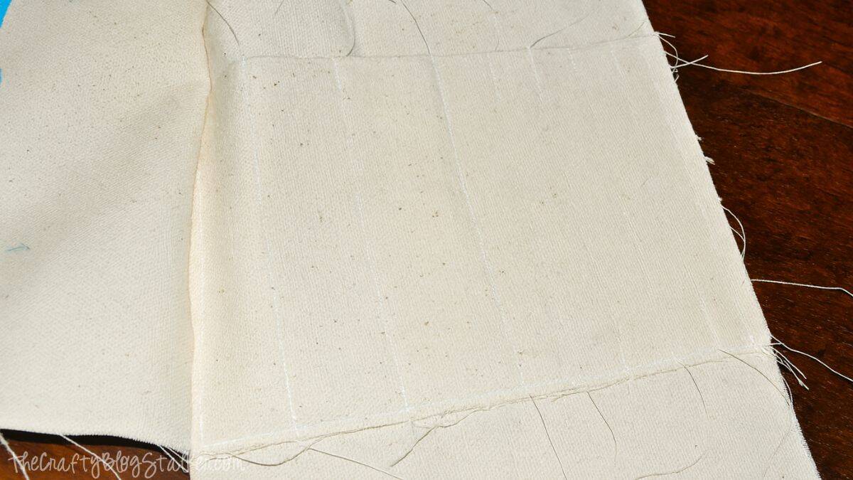 Step 2 Canvas fabric piece with stitched vertical lines forming narrow pockets for holding crochet hooks in a handmade yarn tote bag.