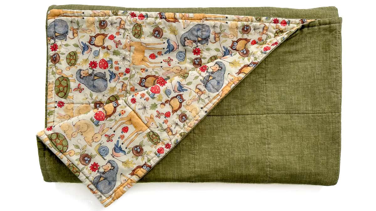 Completed baby blanket folded to display green backing and woodland animal print front with visible quilting stitches.