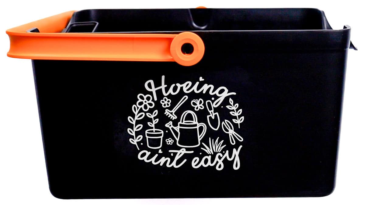 Black gardening bucket with orange handle featuring a gardening-themed vinyl decal on the front showcasing flowers, tools, and a watering can design.