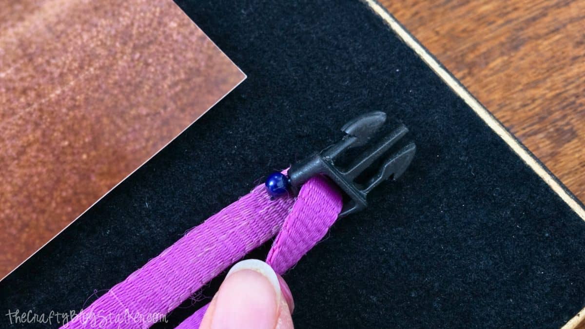 Close-up of a pet collar being fastened to a felt-backed shadow box, with a hand maintaining the collar's position close to a photograph.