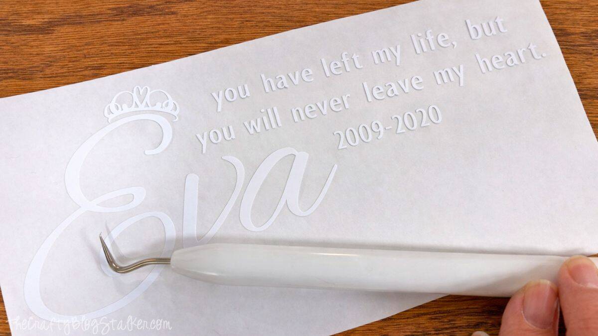 Weeded vinyl memorial design on transfer paper with a hook weeding tool removing excess vinyl from a personalized pet remembrance quote and name.
