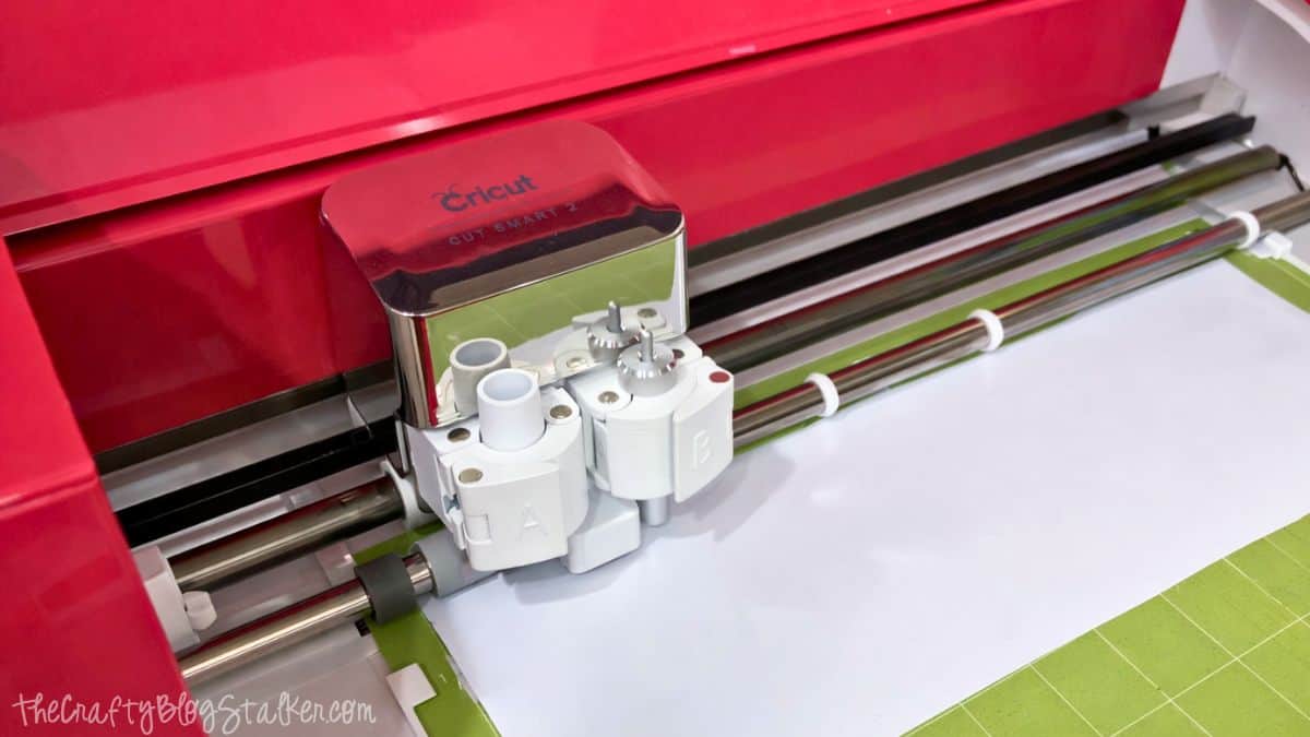 Cricut cutting machine with the blade carriage positioned over a cutting mat, prepared to cut a sheet of material for a craft project.