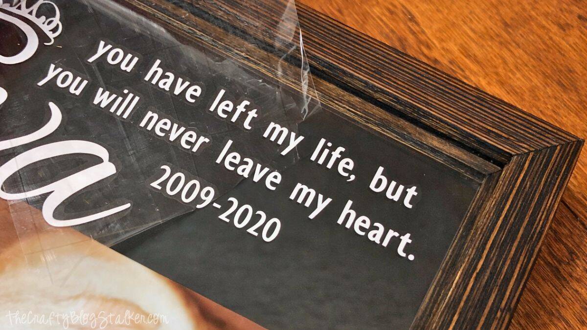 Close-up image of transfer tape being removed from a vinyl memorial quote placed inside a wooden shadow box frame.