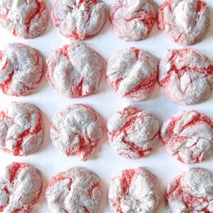 Pink lemonade crinkle cookies baked with cracked tops and a powdered sugar coating, closely arranged on a flat surface.