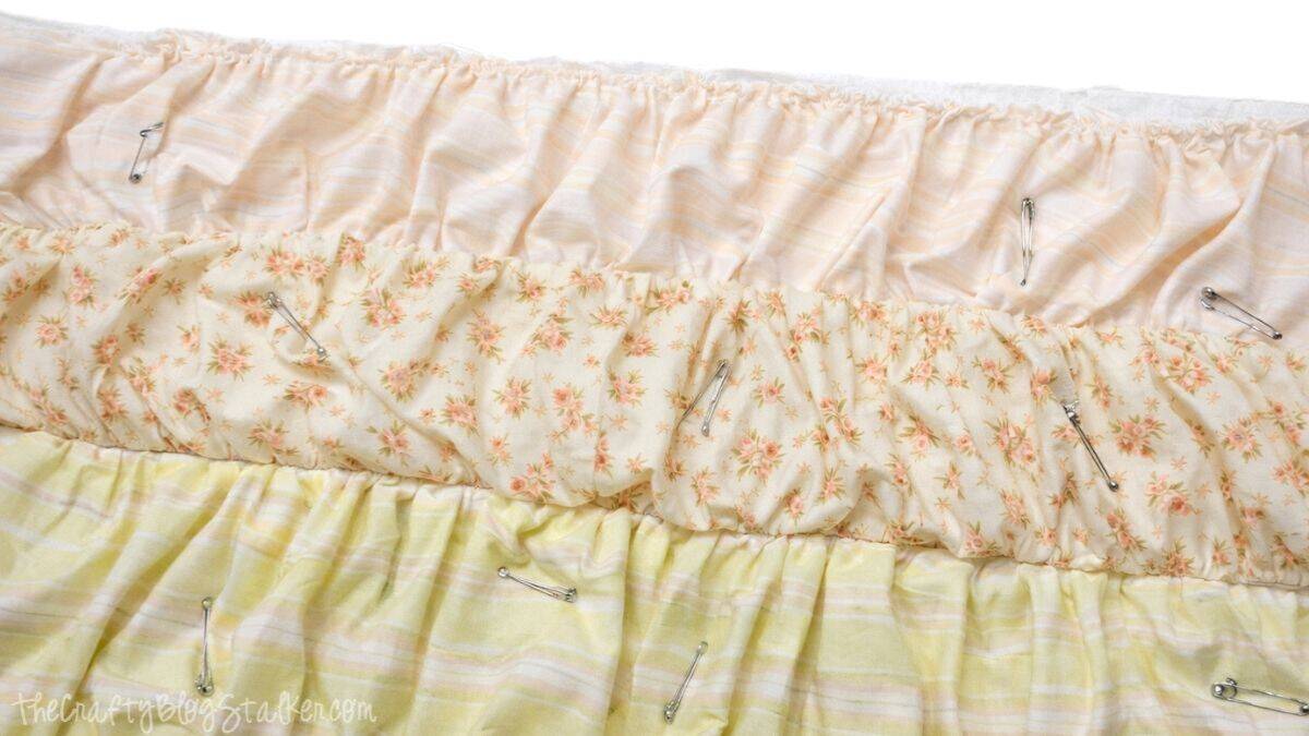 Ruffled quilt top layers fastened together with safety pins, displaying gathered fabric strips held in place before stitching.