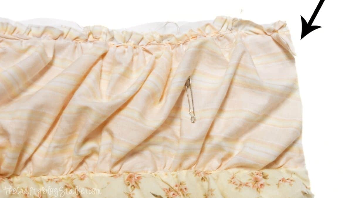 Close-up view of ruffled quilt fabric with additional batting and backing extending beyond the edge, indicating where layers will be trimmed before finishing.