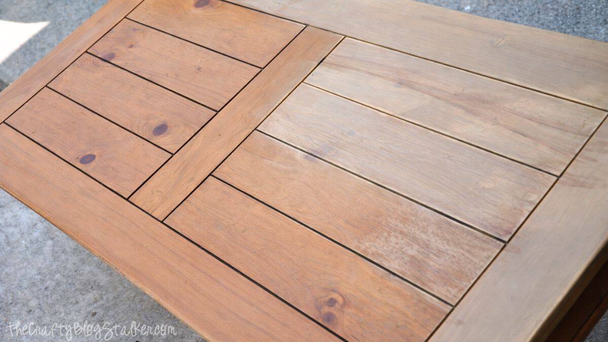 Close-up of a wooden coffee table top featuring a plank-style design, demonstrating the surface being sanded to prepare the wood for refinishing.