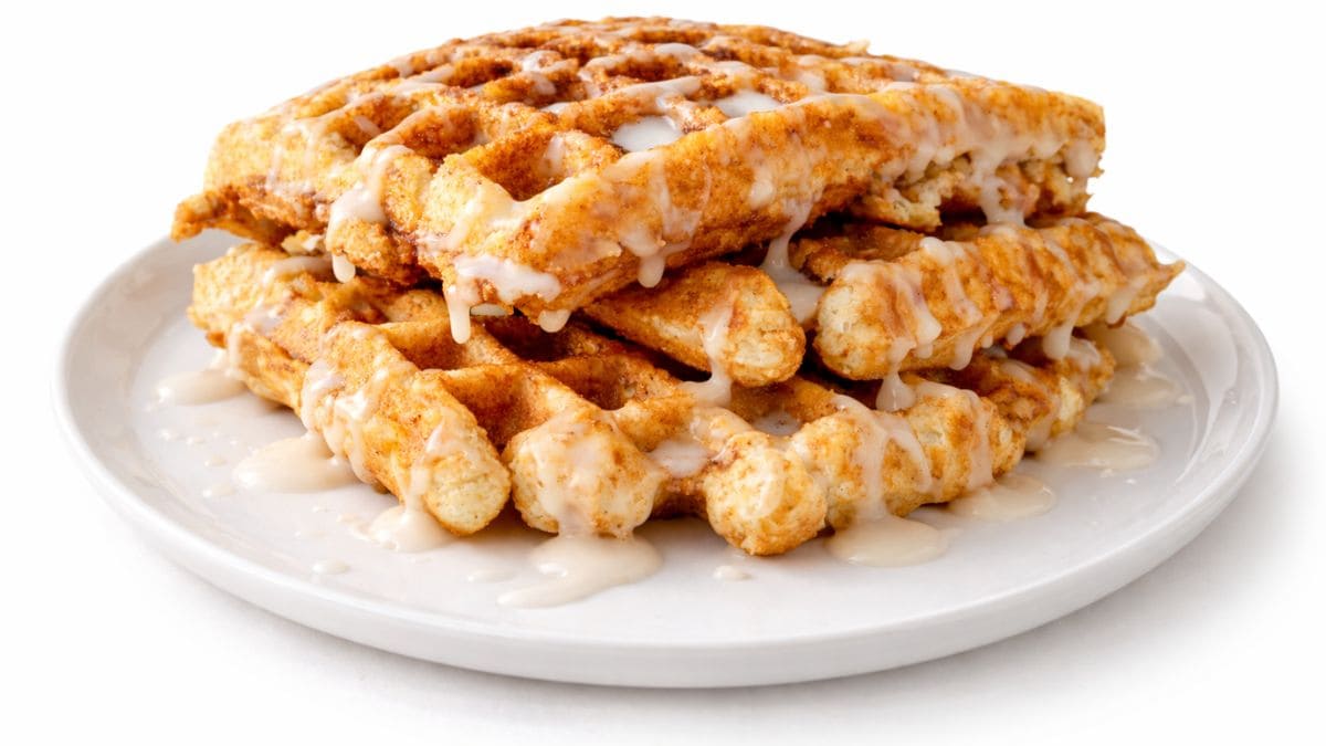 Stack of cinnamon swirl waffles drizzled with icing on a white plate against a clean background.
