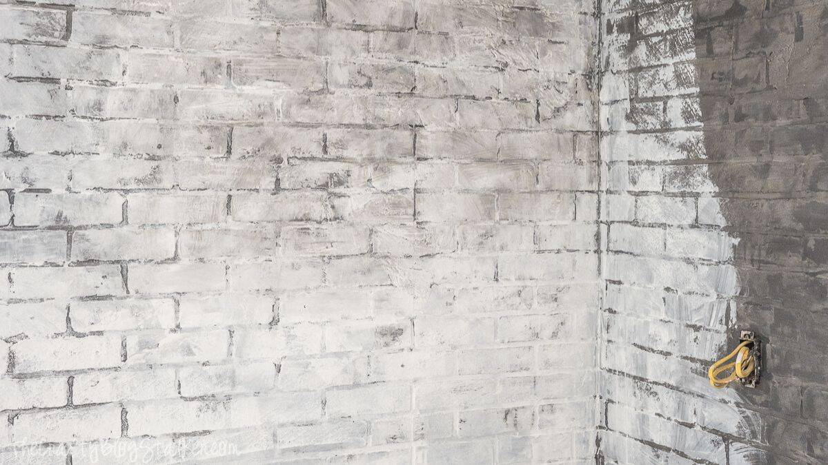 Faux brick wall partially whitewashed, exhibiting layered paint over brick texture with visible mortar lines and a corner section still in progress.