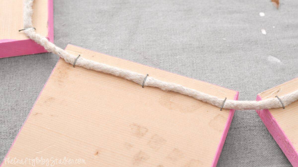 Close-up of rope attached to the rear of wooden banner squares, illustrating how the pieces are interconnected to form a hanging DIY banner.