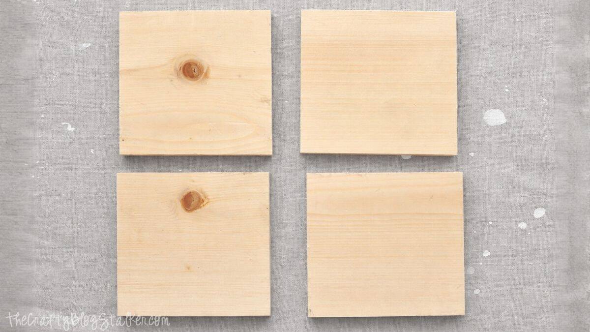 Four unfinished square wooden boards placed in a grid on a fabric-covered working area, ready for a DIY project or home decor.