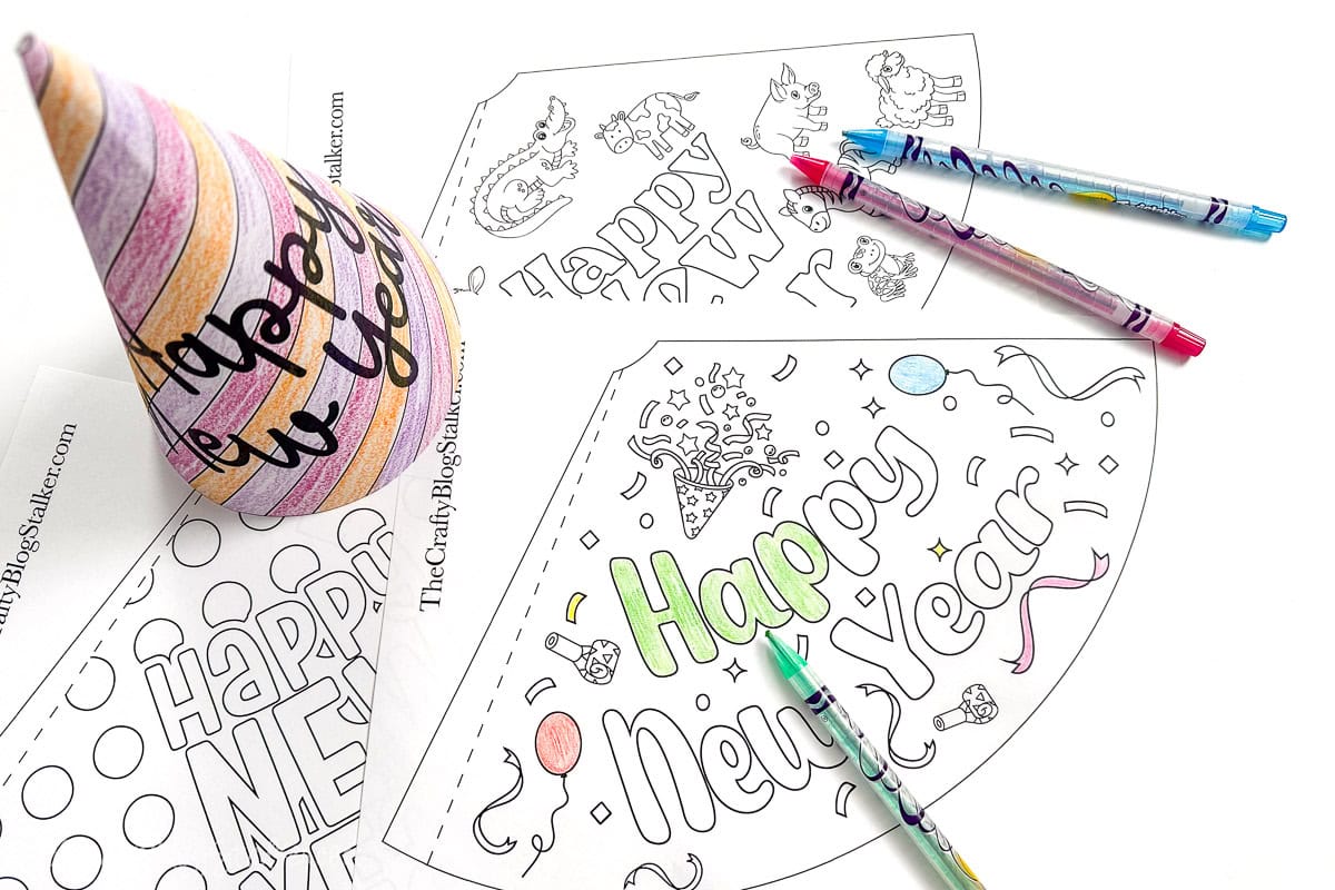 Coloring pages for "Happy New Year" party hats with festive designs, partially colored with crayons, alongside a finished striped hat and markers.