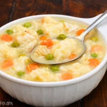 Homemade chicken and dumplings in a white bowl with tender chicken, fluffy dumplings, peas, and carrots in a creamy broth on a wooden table