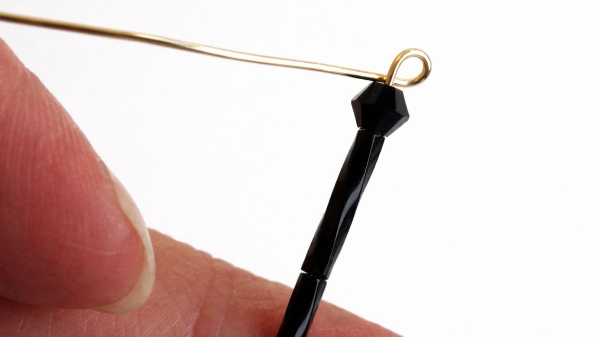 Close-up of a wire leg adorned with beads, featuring a small loop at the end, being held between fingers during the creation of a spider craft.