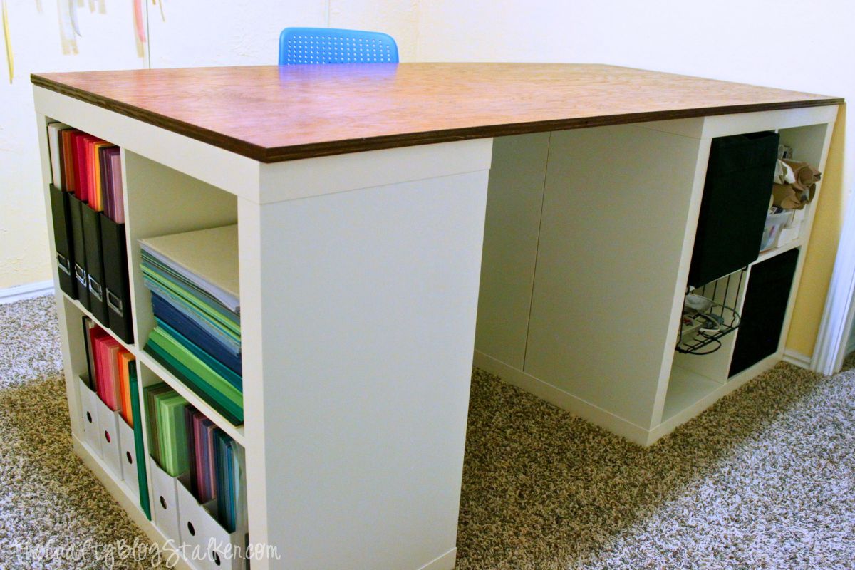 A DIY crafting table constructed from white cube storage units with a stained wooden surface, providing ample workspace and organized storage for crafting materials.