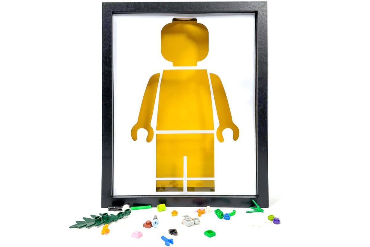 Framed yellow LEGO figure silhouette accompanied by scattered colorful LEGO pieces below, demonstrating an inventive DIY design concept.