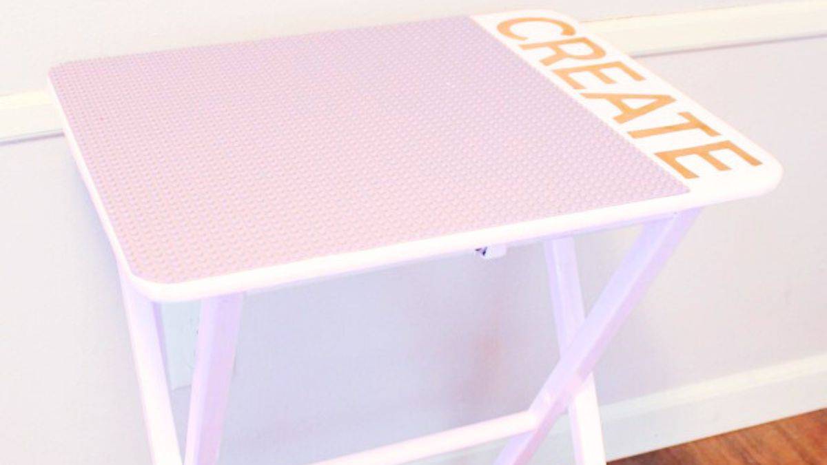 Portable DIY LEGO table with collapsible legs and a studded baseplate surface, designed to facilitate kids in building and playing, depicted set against an indoor wall.