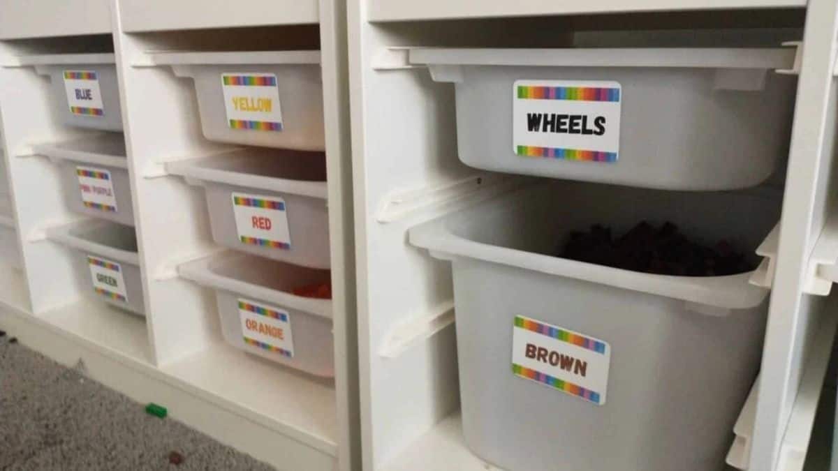 IKEA storage unit equipped with detachable plastic bins utilized to arrange LEGO bricks, classified by color categories and elements like wheels for convenient access during building.