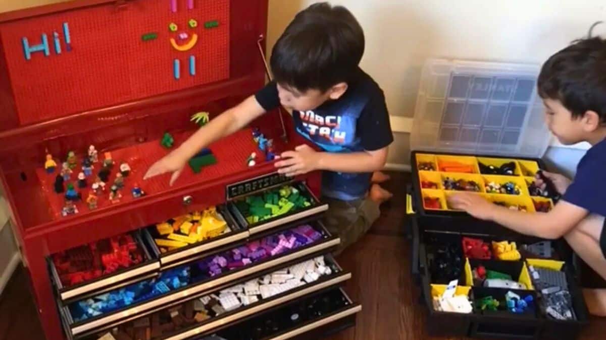 Two youngsters arranging and playing with LEGO blocks using a upcycled tool chest equipped with labeled drawers and compartment organizers for LEGO storage.