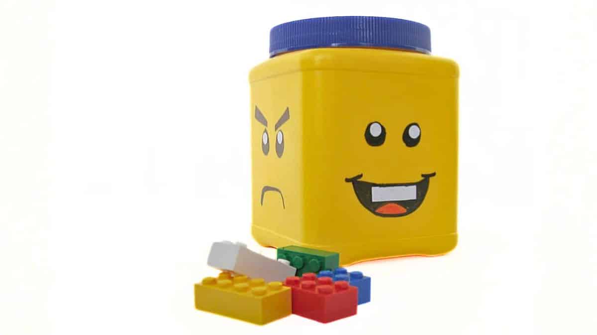 Repurposed plastic container adorned like a LEGO minifigure head, featuring various facial expressions and LEGO bricks scattered nearby.