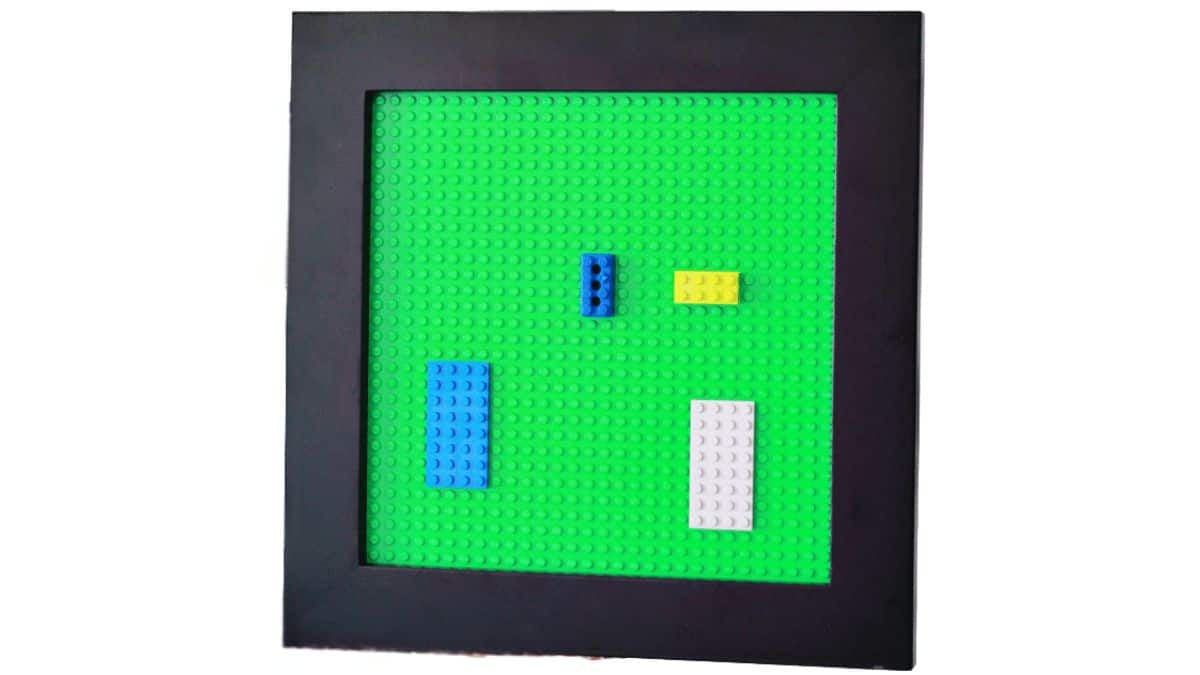 Framed LEGO construction tray featuring a base plate and several LEGO blocks meticulously arranged within, intended as a straightforward play and exhibit surface.