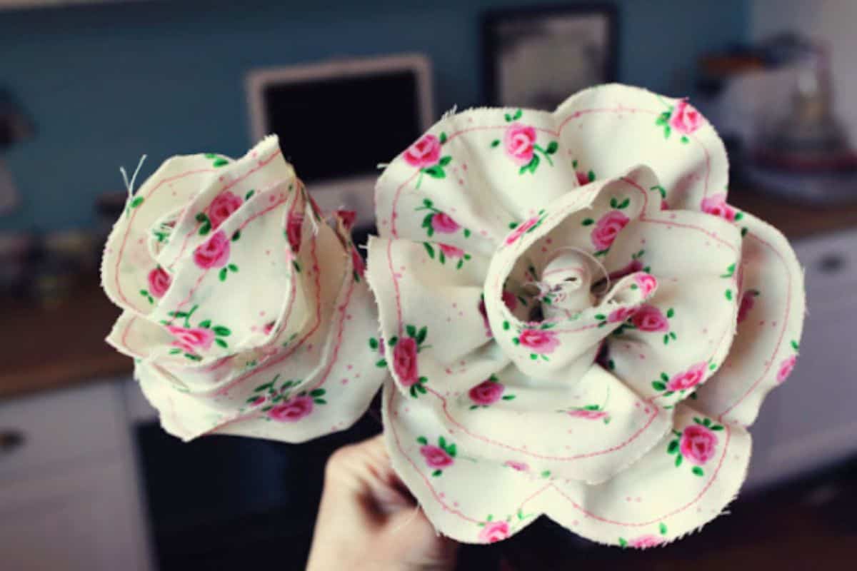 A hand displaying two handcrafted fabric roses made from patterned cotton, showcasing layered petals and stitched edges as a DIY fabric flower project.
