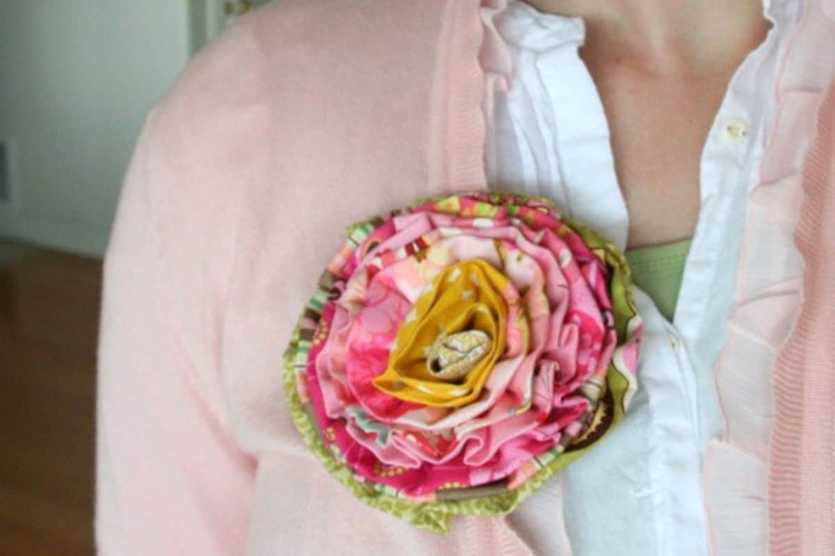 Handmade layered fabric flower brooch secured to a cardigan, designed from patterned fabric strips featuring a folded fabric center.
