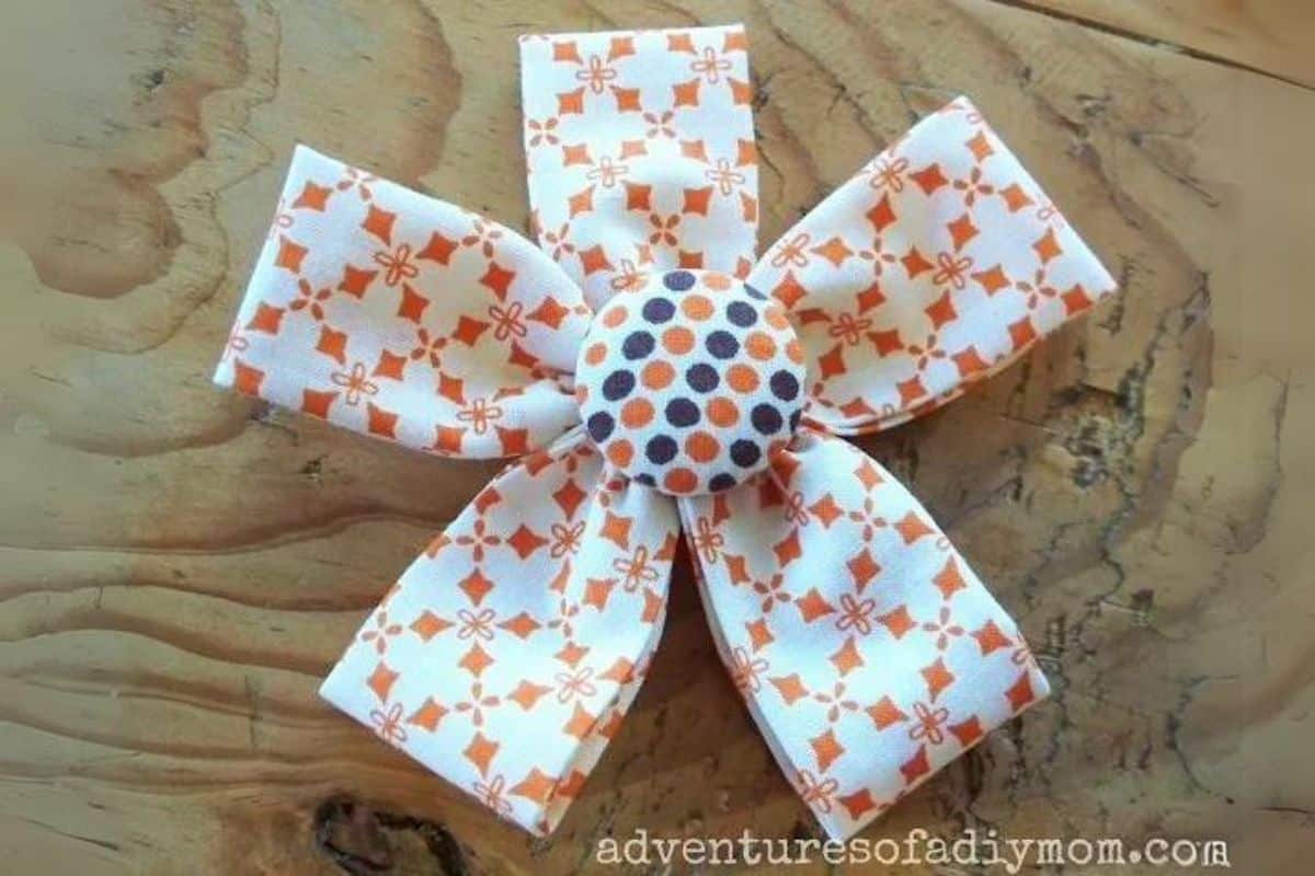 Fabric flower crafted from folded patterned cotton strips featuring five petals and a covered button center, showcased on a wooden surface.