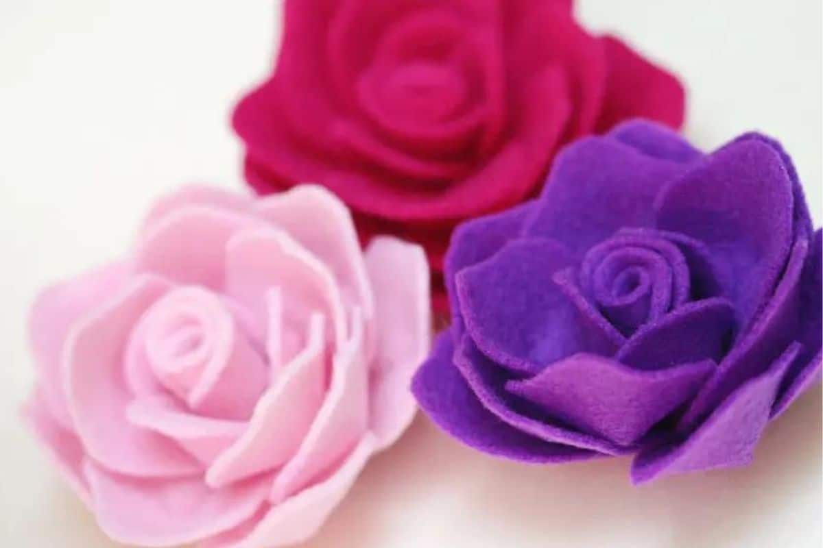 Three handcrafted felt roses featuring layered petals, placed together on a light background as a simple crafting or embellishing example.
