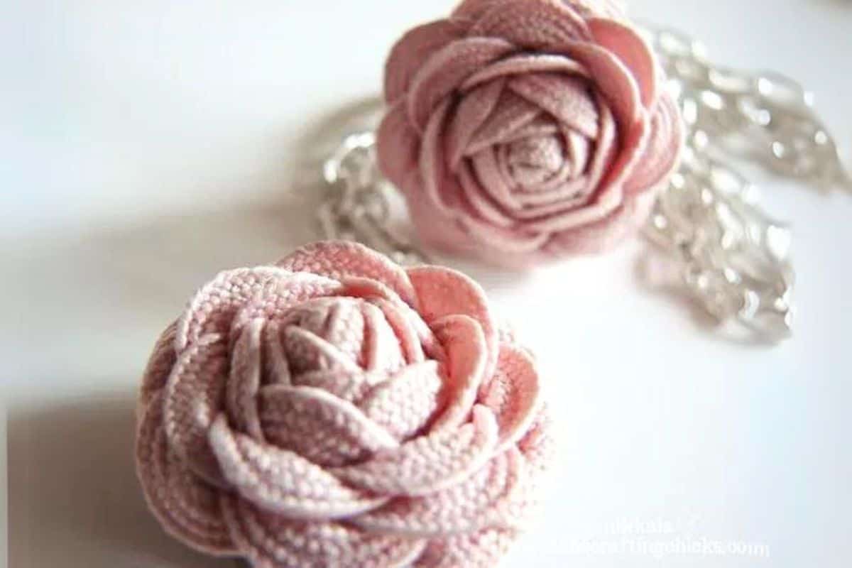 Two artisan rick rack rosette flowers affixed to chain jewelry, showcased in close-up as fabric flower adornments against a white surface.