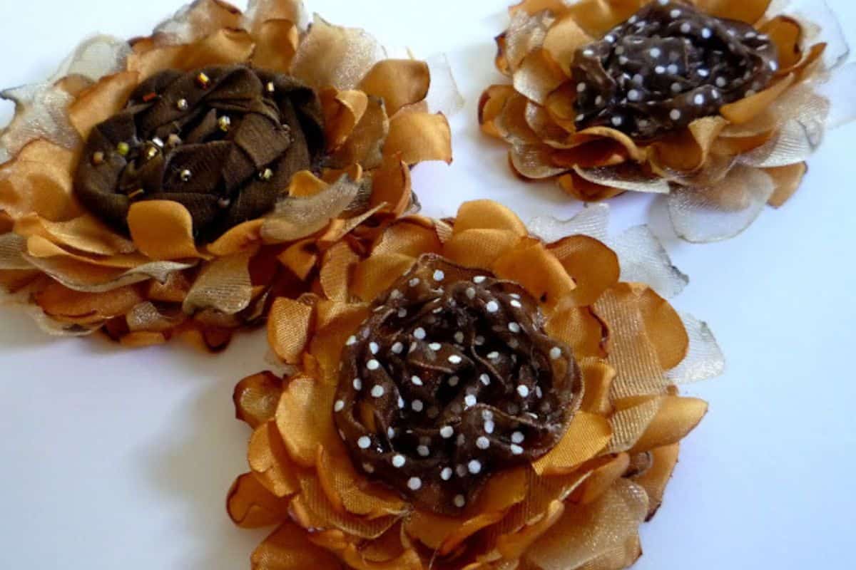 Three handmade fabric sunflowers showing layered fabric petals and textured centers, closely arranged on a white background as a craft undertaking.